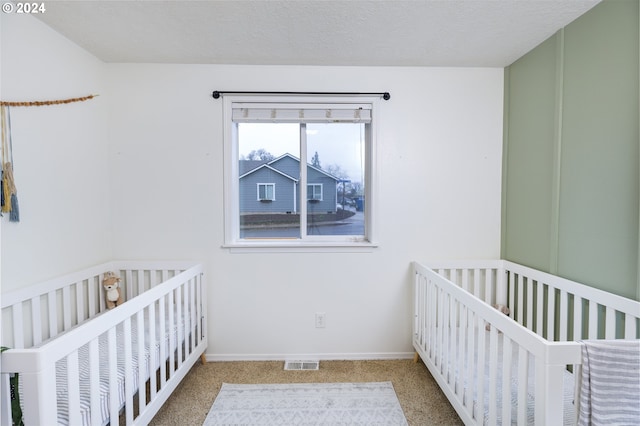 unfurnished bedroom featuring baseboards, visible vents, a textured ceiling, carpet flooring, and a nursery area