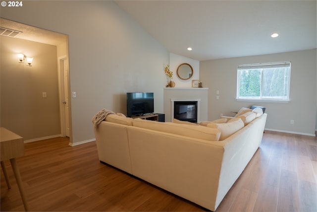 living area featuring lofted ceiling, a glass covered fireplace, visible vents, and light wood-style floors