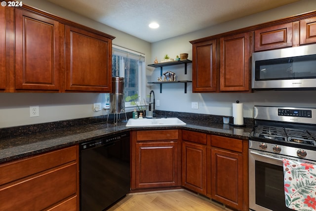 kitchen with light wood finished floors, dark stone countertops, stainless steel appliances, open shelves, and a sink