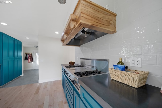 kitchen with blue cabinetry, tasteful backsplash, premium range hood, light hardwood / wood-style floors, and stainless steel cooktop