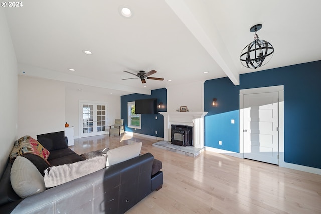 living room featuring french doors, ceiling fan with notable chandelier, light hardwood / wood-style flooring, beamed ceiling, and a wood stove