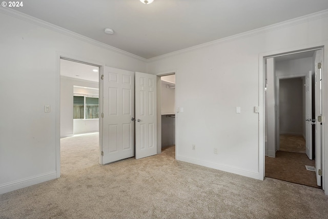 unfurnished bedroom with light carpet, a walk in closet, ornamental molding, and a closet