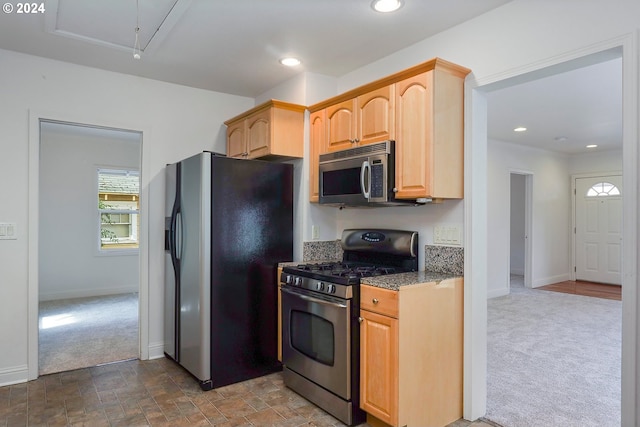 kitchen featuring dark carpet, appliances with stainless steel finishes, dark stone counters, and light brown cabinets