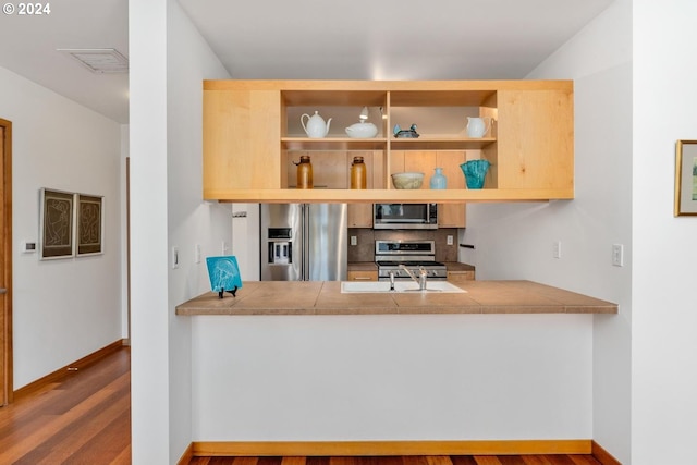 kitchen featuring decorative backsplash, appliances with stainless steel finishes, sink, hardwood / wood-style floors, and tile counters