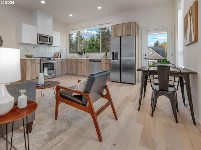 kitchen with white cabinets, a healthy amount of sunlight, appliances with stainless steel finishes, and light hardwood / wood-style flooring