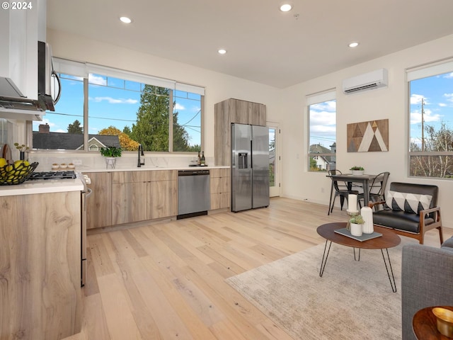 kitchen featuring a wall mounted air conditioner, plenty of natural light, light wood-type flooring, and stainless steel appliances