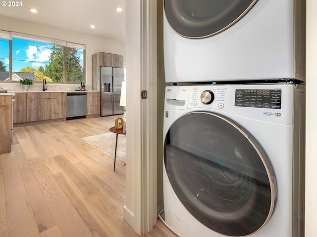 laundry room with light wood-type flooring, sink, and stacked washer and clothes dryer