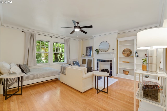 living room with light hardwood / wood-style floors, built in features, a tile fireplace, and ceiling fan