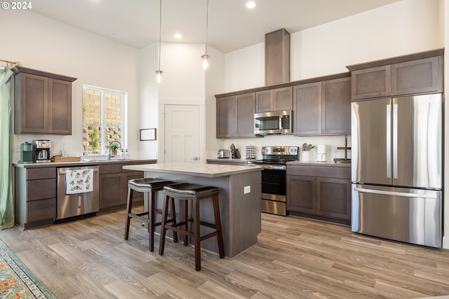 kitchen featuring a center island, appliances with stainless steel finishes, light wood-type flooring, a towering ceiling, and decorative light fixtures