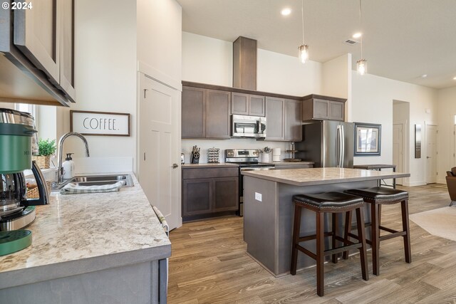 kitchen featuring a breakfast bar, pendant lighting, stainless steel appliances, light hardwood / wood-style flooring, and sink