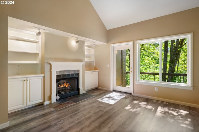 unfurnished living room featuring dark hardwood / wood-style floors, high vaulted ceiling, a tiled fireplace, and built in shelves