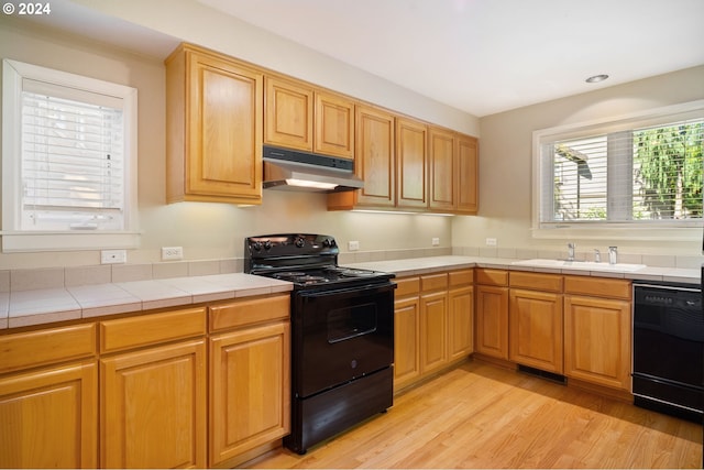 kitchen featuring sink, black appliances, light hardwood / wood-style flooring, and tile countertops