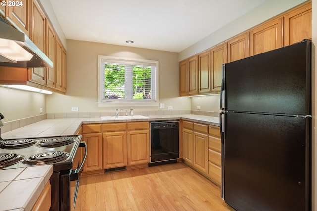 kitchen featuring sink, light wood-type flooring, black appliances, and tile countertops