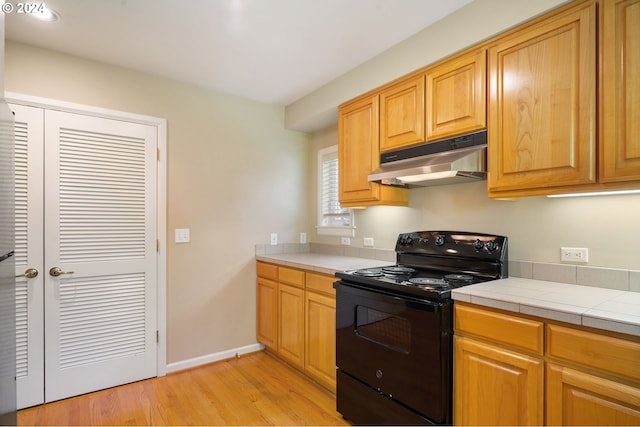 kitchen with light wood-type flooring, black range with electric cooktop, and tile countertops