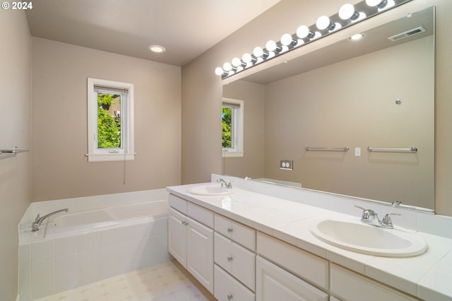 bathroom featuring tile flooring, a relaxing tiled bath, vanity with extensive cabinet space, and dual sinks