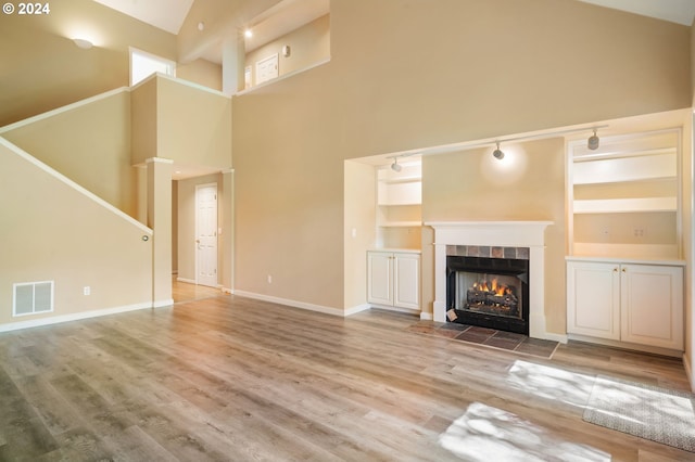 unfurnished living room with a fireplace, built in features, rail lighting, wood-type flooring, and a high ceiling