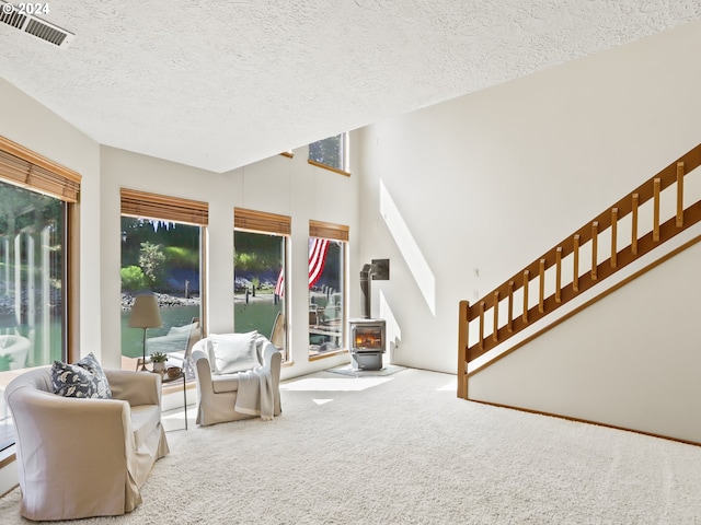 living area featuring carpet, a wood stove, a textured ceiling, and high vaulted ceiling