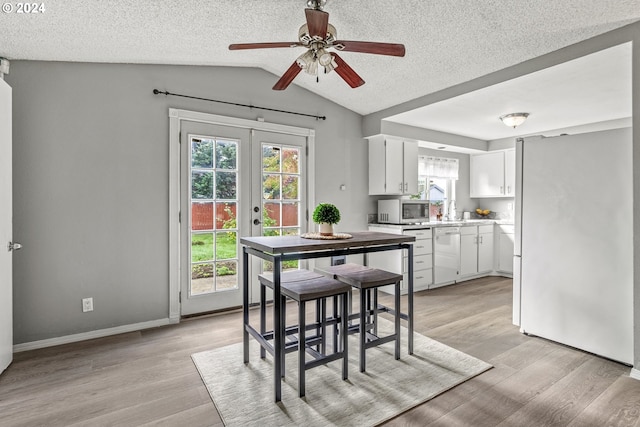 dining space with french doors, light hardwood / wood-style flooring, vaulted ceiling, a textured ceiling, and ceiling fan