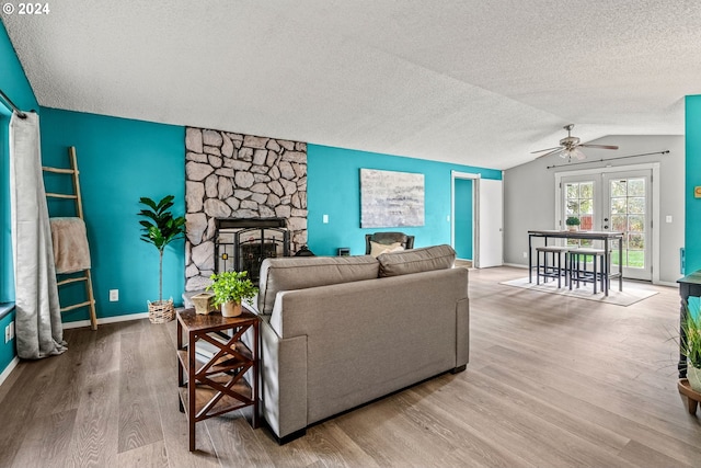 living room featuring lofted ceiling, a stone fireplace, a textured ceiling, light hardwood / wood-style floors, and ceiling fan