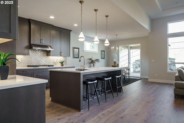 kitchen featuring pendant lighting, an island with sink, sink, a kitchen breakfast bar, and decorative backsplash