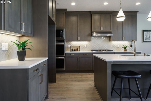 kitchen with sink, backsplash, hanging light fixtures, light hardwood / wood-style floors, and stainless steel appliances