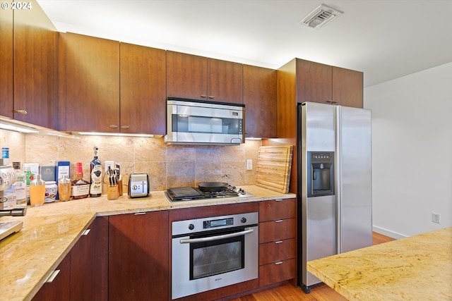 kitchen featuring light stone countertops, appliances with stainless steel finishes, tasteful backsplash, and light hardwood / wood-style flooring