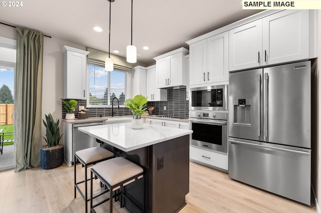 kitchen with pendant lighting, a center island, light hardwood / wood-style flooring, appliances with stainless steel finishes, and white cabinetry