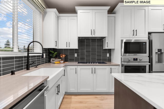 kitchen featuring light stone countertops, appliances with stainless steel finishes, backsplash, light wood-type flooring, and white cabinets