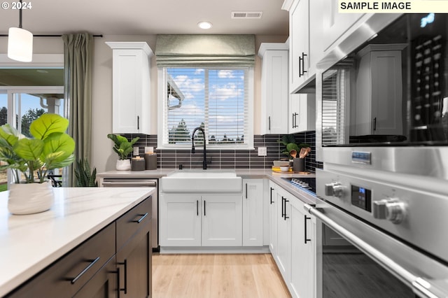 kitchen with tasteful backsplash, white cabinetry, hanging light fixtures, and appliances with stainless steel finishes