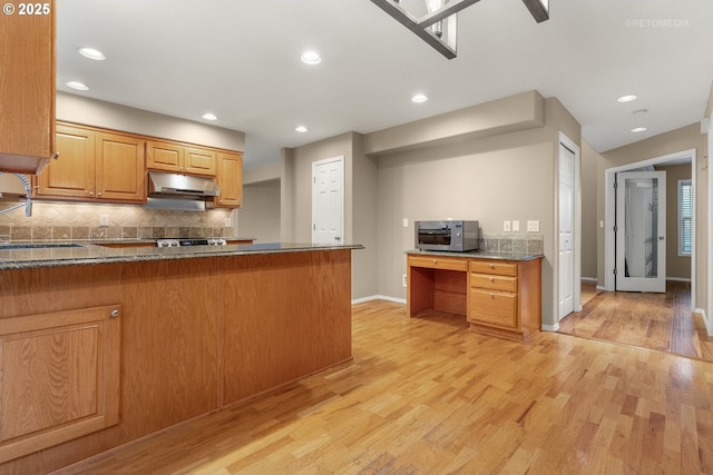 kitchen featuring dark stone countertops, kitchen peninsula, sink, light hardwood / wood-style flooring, and backsplash