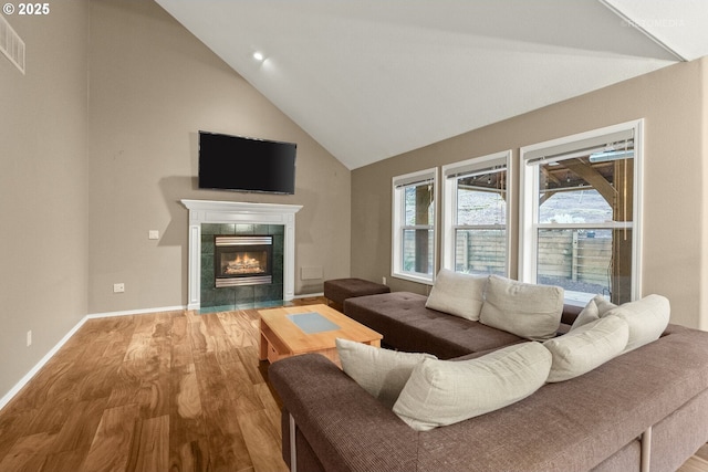 living room with a tiled fireplace, vaulted ceiling, and hardwood / wood-style floors