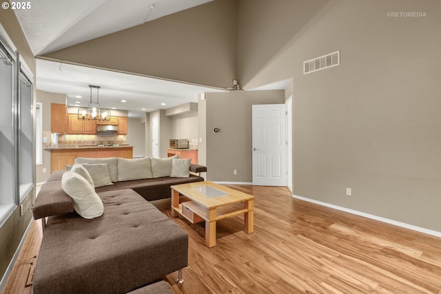 living room with a notable chandelier, light hardwood / wood-style flooring, and vaulted ceiling