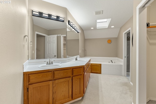 bathroom with a washtub, a textured ceiling, vaulted ceiling with skylight, and vanity