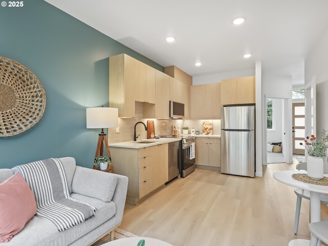 kitchen with sink, light wood-type flooring, stainless steel appliances, light brown cabinets, and decorative backsplash