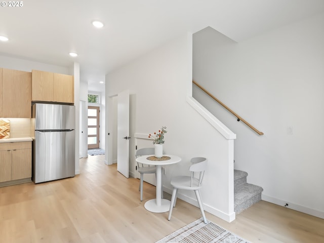 kitchen with light wood-type flooring, tasteful backsplash, stainless steel refrigerator, and light brown cabinets