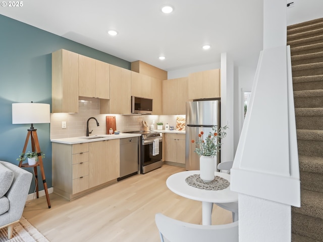 kitchen featuring appliances with stainless steel finishes, light brown cabinetry, light hardwood / wood-style floors, backsplash, and sink