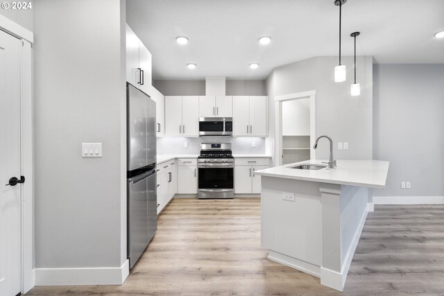 kitchen with stainless steel appliances, decorative light fixtures, sink, light hardwood / wood-style floors, and white cabinets