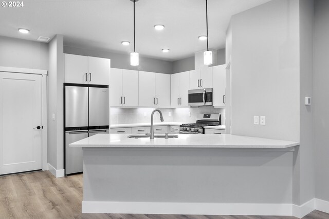 kitchen with white cabinets, light hardwood / wood-style flooring, sink, appliances with stainless steel finishes, and decorative light fixtures