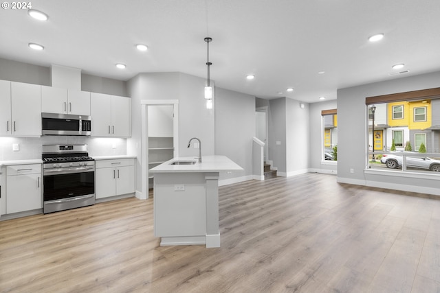 kitchen with white cabinetry, sink, appliances with stainless steel finishes, hanging light fixtures, and light hardwood / wood-style flooring