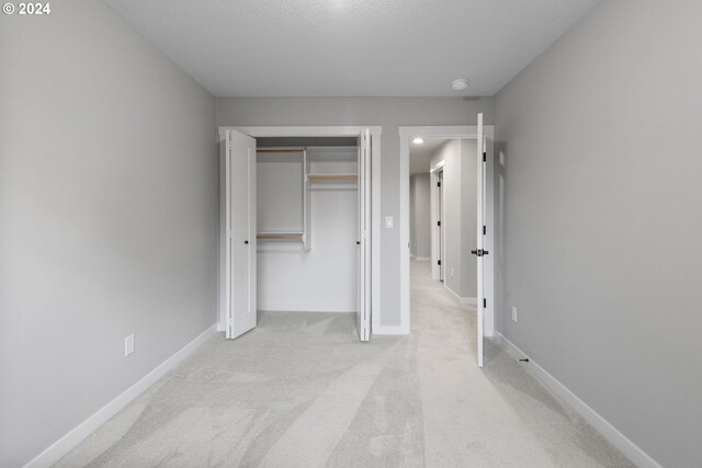 unfurnished bedroom with a textured ceiling, light carpet, and a closet