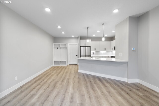 kitchen with stainless steel appliances, sink, hanging light fixtures, white cabinets, and light wood-type flooring