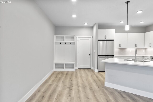 kitchen with white cabinetry, hanging light fixtures, stainless steel fridge, and light wood-type flooring