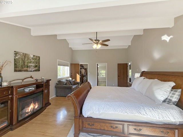 bedroom with light wood-type flooring, ceiling fan, vaulted ceiling with beams, and a walk in closet