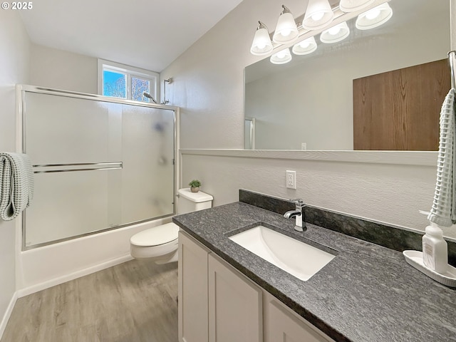 full bathroom with hardwood / wood-style floors, toilet, combined bath / shower with glass door, and vanity