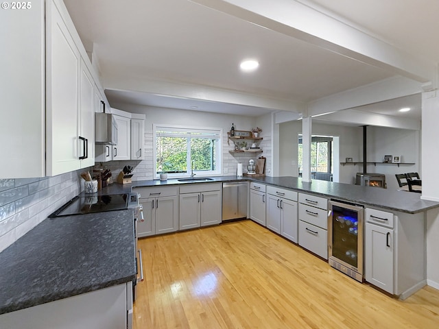 kitchen with kitchen peninsula, light hardwood / wood-style flooring, wine cooler, backsplash, and appliances with stainless steel finishes