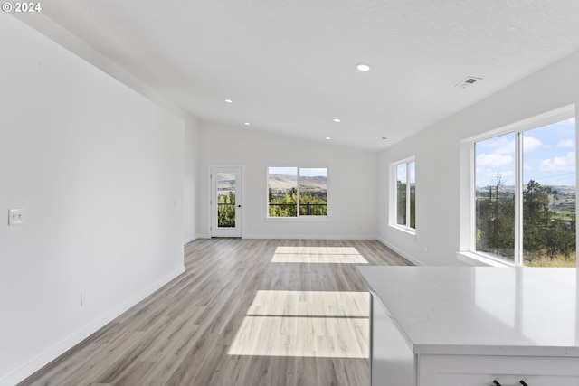 unfurnished living room with a textured ceiling, lofted ceiling, and light hardwood / wood-style flooring