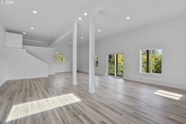 unfurnished living room featuring light hardwood / wood-style flooring, a high ceiling, and beamed ceiling