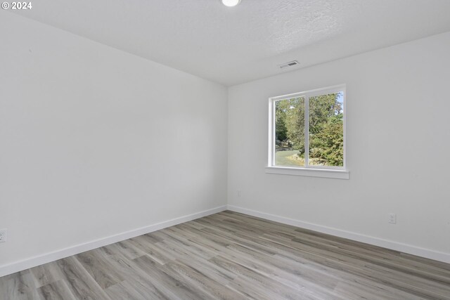 empty room with light wood-type flooring and a textured ceiling