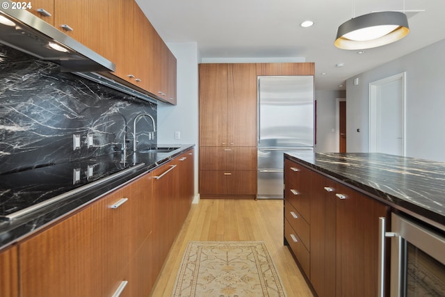 kitchen with sink, tasteful backsplash, built in refrigerator, light hardwood / wood-style flooring, and ventilation hood