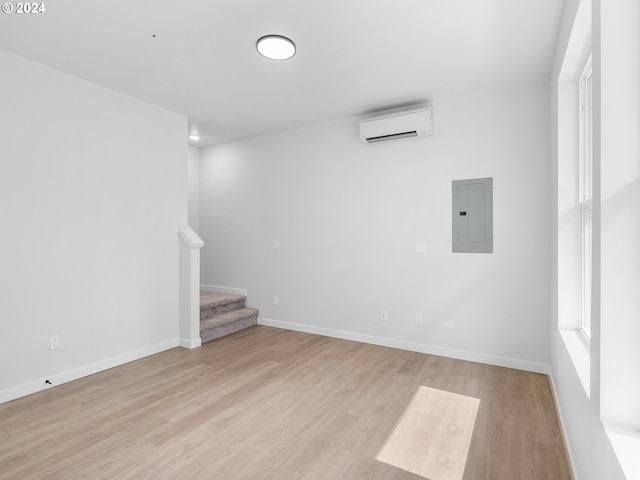 unfurnished room with electric panel, light hardwood / wood-style floors, and a wall mounted air conditioner